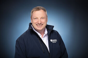 Portraitbild von Volker Rozek vor einem Blau Weißen Hintergrund mit Blauer Jacke
